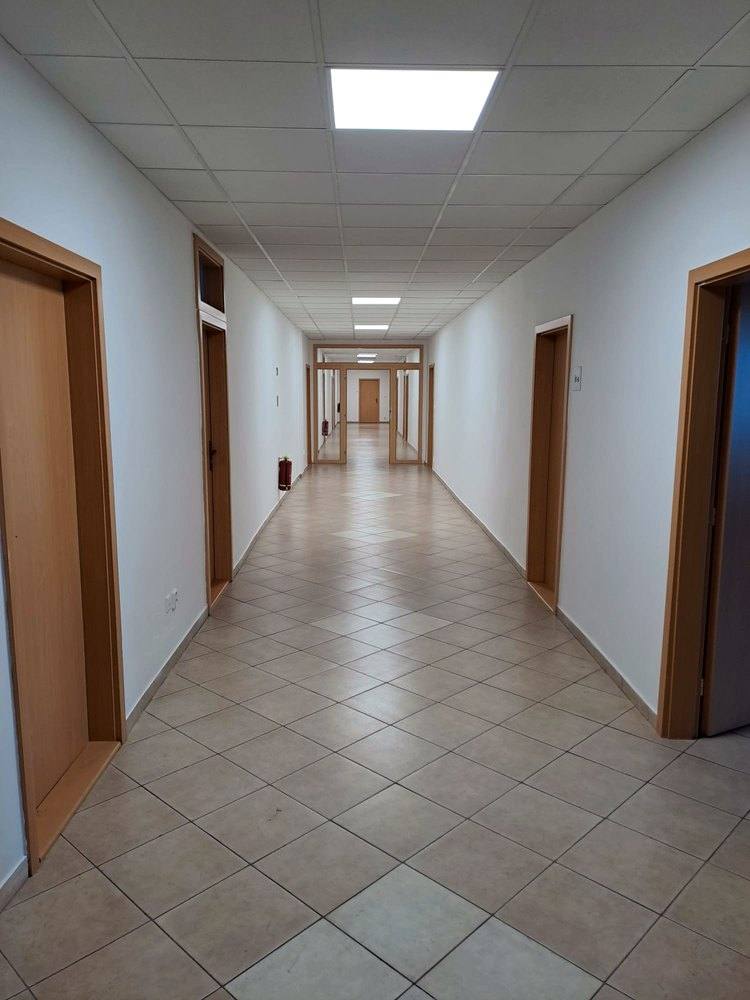 Chodba kancelárskeho podlažia s béžovou dlažbou a drevenými dverami po oboch stranách